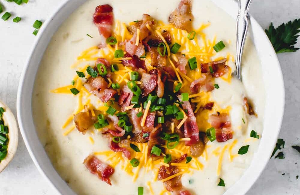 Loaded baked potato soup in a white bowl with a spoon garnished with chopped bacon, cheese and onions.